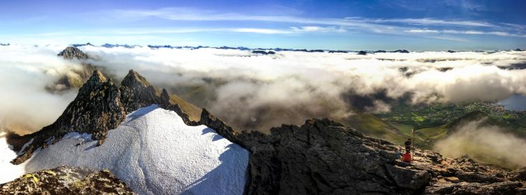 A panoramic view from Saudehornet showcasing a sunset with low-hanging clouds over the rugged terrain.