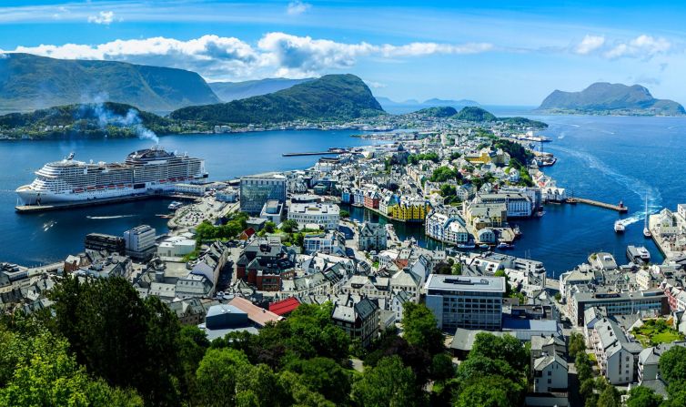 Aerial view of Ålesund, Norway, featuring colorful buildings, harbor, and mountainous backdrop.