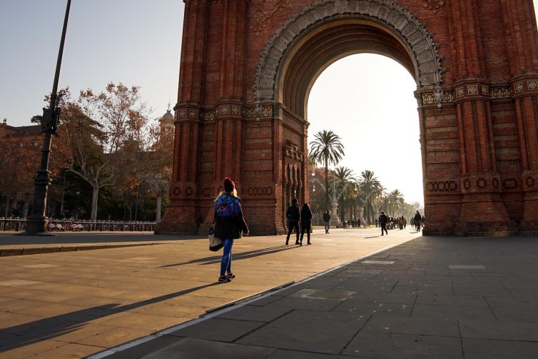 Woman walking past the Arc de Triomf in Barcelona, with palm trees in the background.