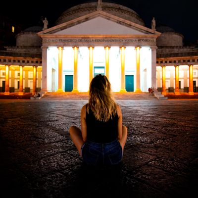 A figure seated in front of illuminated historic architecture in Naples at night.