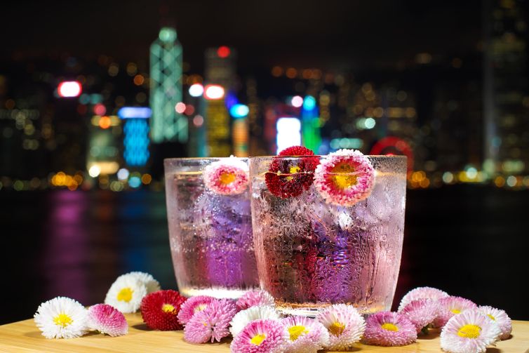 Two flower-adorned drinks with condensation in front of Hong Kong skyline lights.