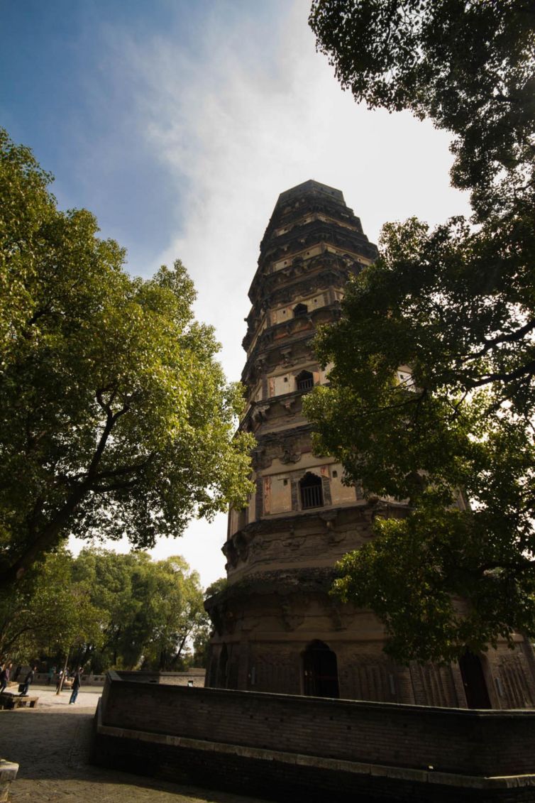 Huqiu Tower in Suzhou, China, surrounded by green trees under a bright sky.