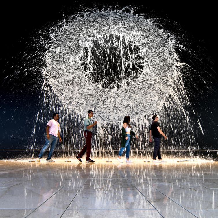 People walking past a vibrant fountain art installation in Dallas, Texas.