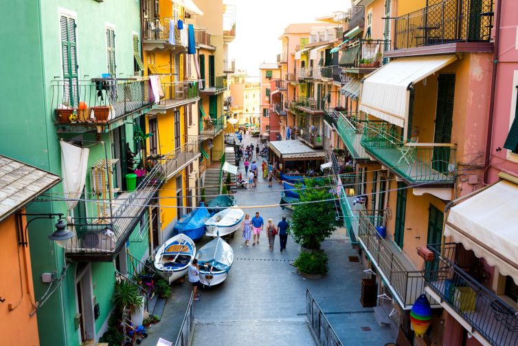 Colorful street scene in Riomaggiore, Italy, featuring boats and lively balconies.