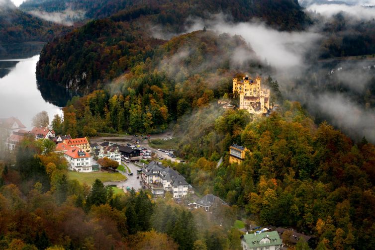 Aerial view of a castle surrounded by autumn foliage and mist in Bavaria, Germany.
