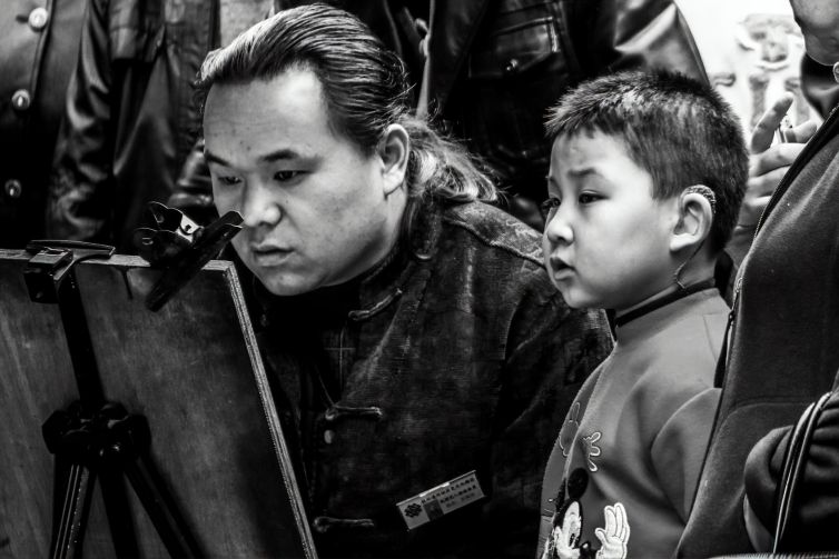 A black and white portrait of a painter and his boy observing painting techniques.