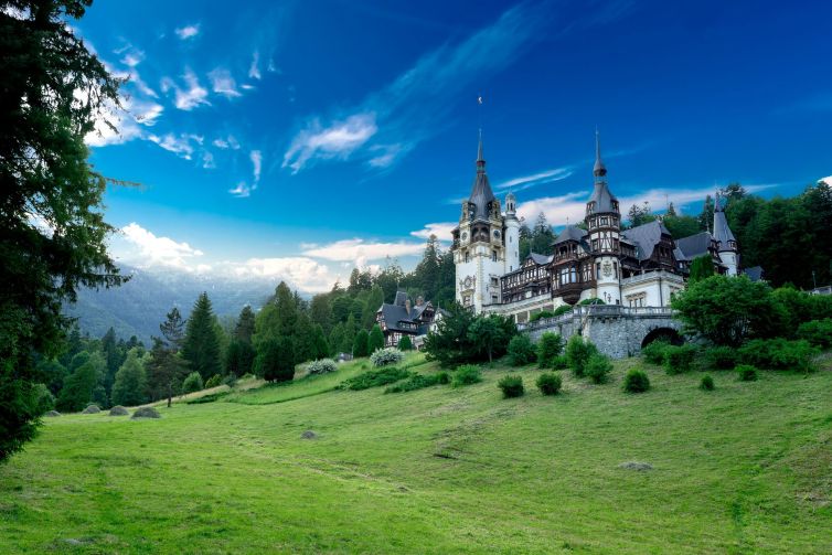 Majestic castle in Romania's Prahova Valley, surrounded by lush greenery and blue skies.