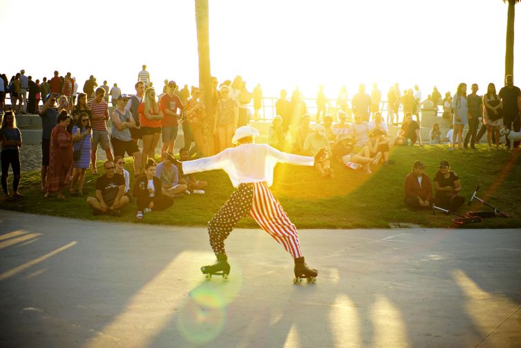 Colorful roller skater performing in front of an audience at Venice Beach during sunset.