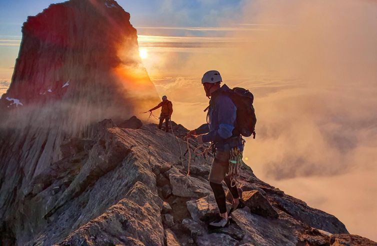 Two climbers navigating a rocky ridge at sunset in Norway.