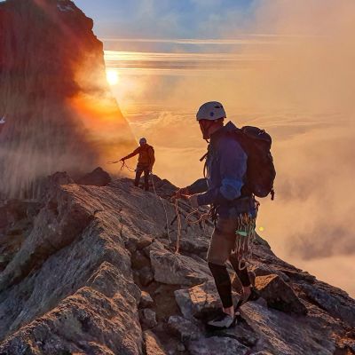 Two climbers navigating a rocky ridge at sunset in Norway.
