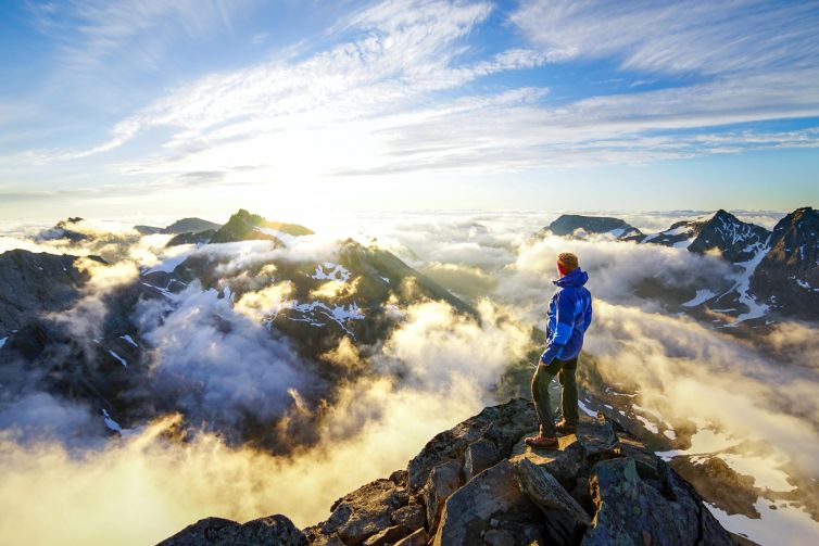Person standing on rocky ledge overlooking the clouds and mountains of Norangsfjorden, Norway.