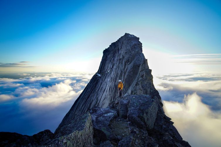 Dramatic mountain peak in Kjøpsvik, Norway set against a clear sky and clouds.