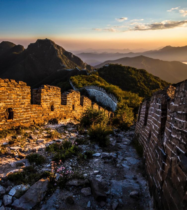 Golden sunset over the ancient Great Wall, surrounded by mountains.