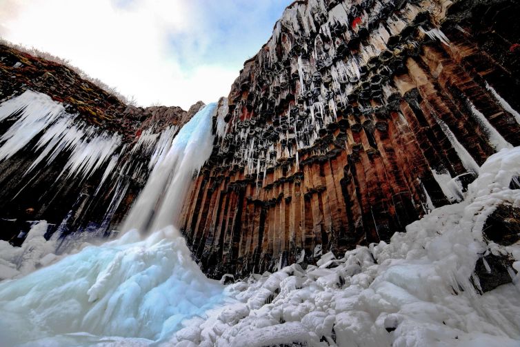 Cascading waterfall in Fagurhólsmýri, Iceland, surrounded by icy formations.