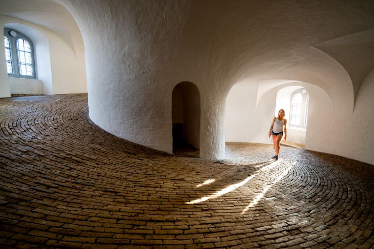 Woman walking on a winding brick path in a bright, curved interior in Copenhagen.