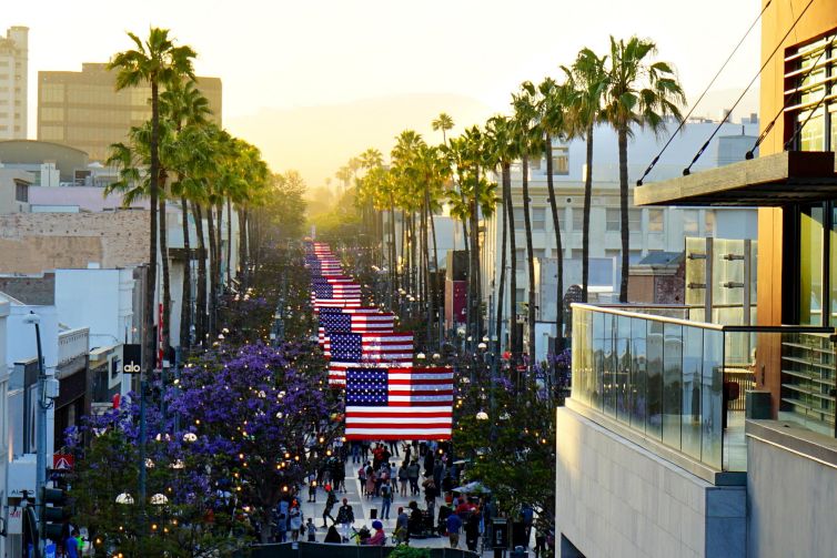 Santa Monica street lined with palm trees and American flags at sunset.