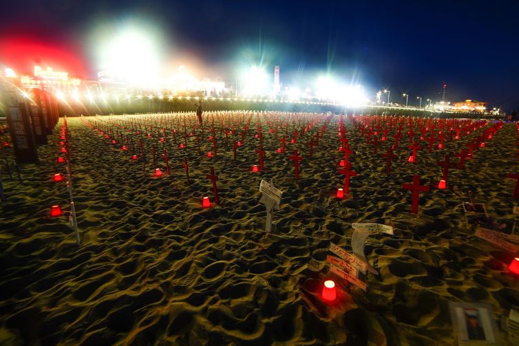 Santa Monica beach tribute featuring red crosses and candles at night.