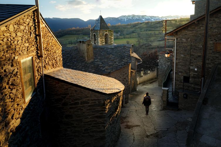 A tranquil Girona street at sunset, featuring stone buildings and distant mountains.