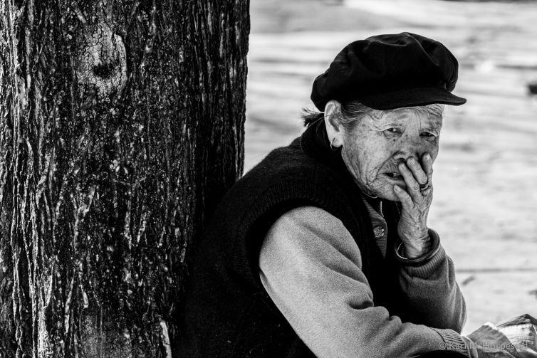 A portrait of an elderly Chinese woman resting by a tree, showcasing the wrinkles of age.